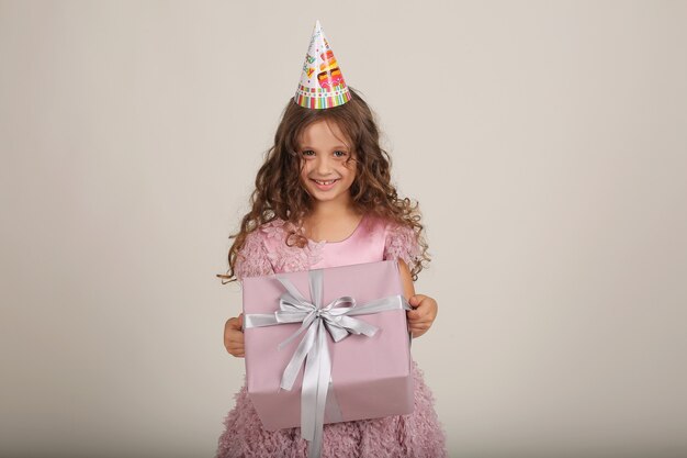 una hermosa niña con cabello rizado con un vestido rosa con una caja de regalo en sus manos es una fiesta