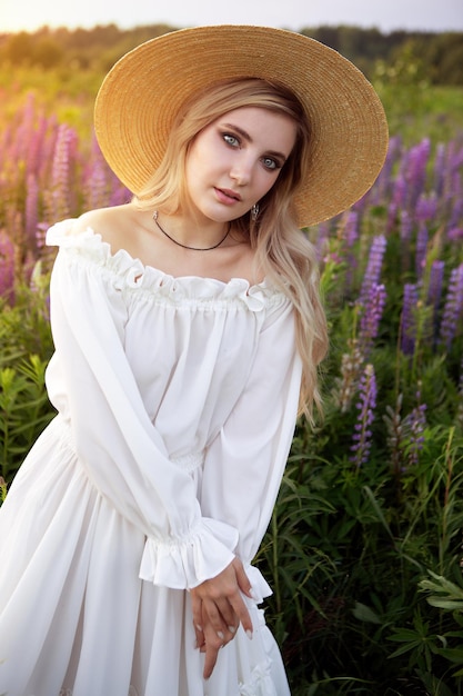 Una hermosa niña de cabello rubio con elegante ropa blanca y un sombrero de paja en un campo de verano