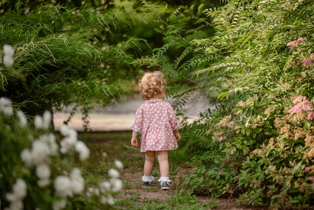 La hermosa niña con un cabello rubio rizado en un paseo por el parque en un cálido día de verano