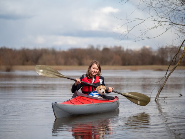 Una hermosa niña y un cachorro de Jack Russell Terrier viajan en un kayak rojo.