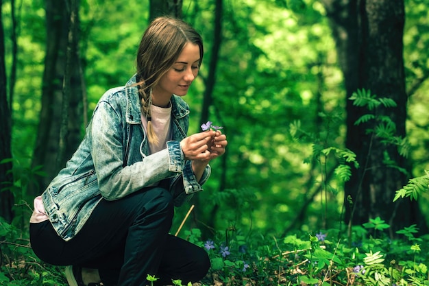 una hermosa niña camina por el bosque verde en la estación cálida y recoge flores