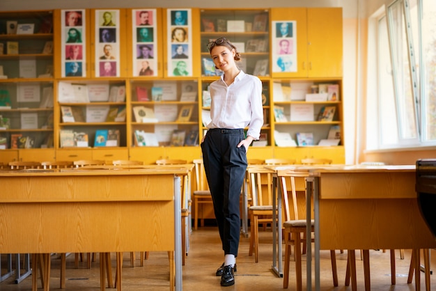 Una hermosa niña en una camisa blanca se encuentra en el aula entre los escritorios