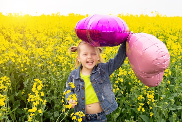 Una hermosa niña en un campo de colza sonriendo en un día de verano con corazones rosas en la mano