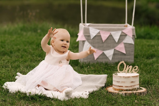 Una hermosa niña en una canasta con un globo y un pastel celebra su primer cumpleaños