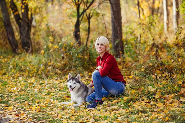 Hermosa niña caucásica juega con perro husky en bosque otoñal