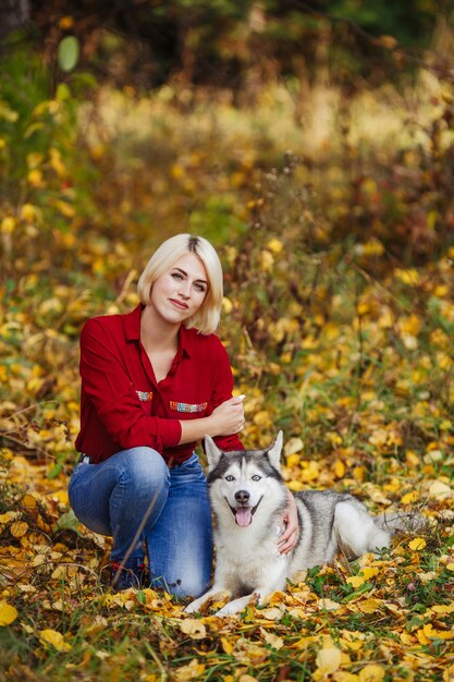Hermosa niña caucásica juega con perro husky en bosque otoñal