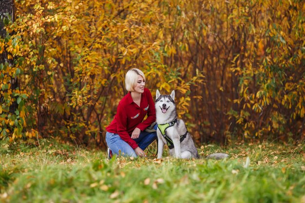 Hermosa niña caucásica juega con perro husky en bosque otoñal