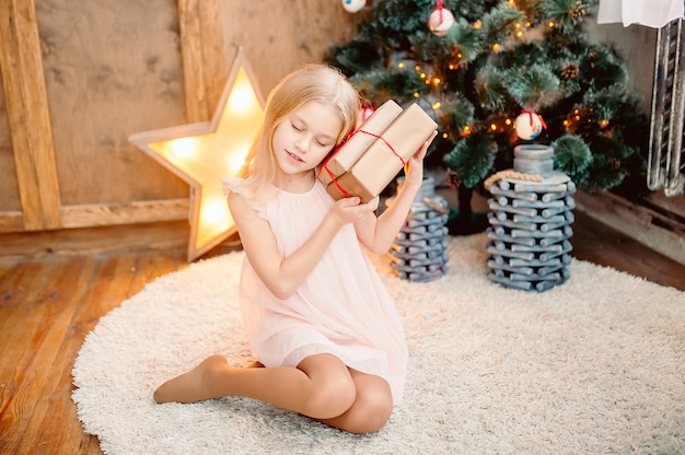 Hermosa niña cerca de un árbol de Navidad y una estrella brillante sostiene un regalo, en un interior de año nuevo brillante. Navidad