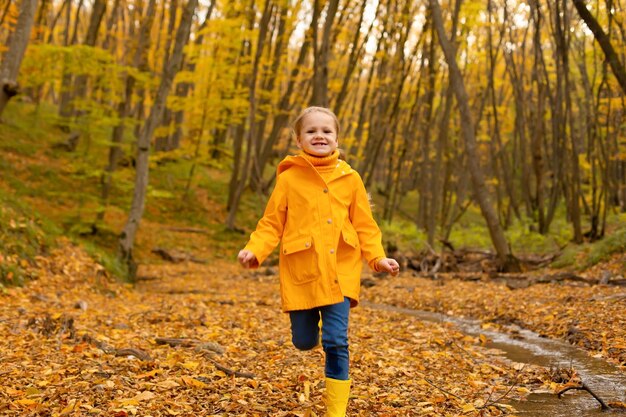 Una hermosa niña con una chaqueta amarilla y botas camina por el bosque urbano de otoño.