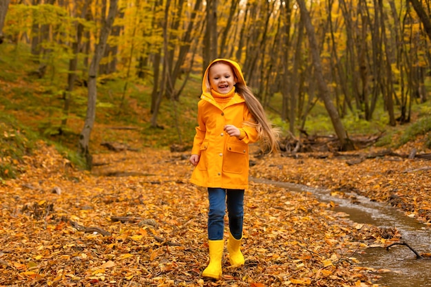 Una hermosa niña con una chaqueta amarilla y botas camina por el bosque urbano de otoño.