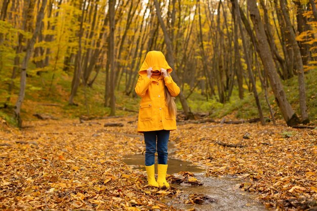 Una hermosa niña con una chaqueta amarilla y botas camina por el bosque urbano de otoño.