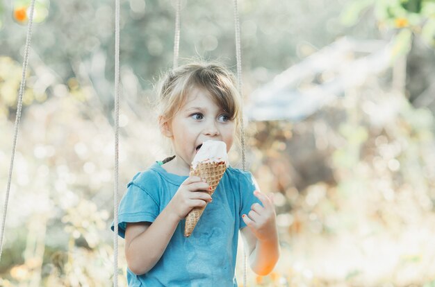 Una hermosa niña de cinco años, comiendo helado al aire libre, sentada en un columpio, el cono con fruta