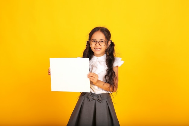 Hermosa niña colegiala con cabello oscuro una niña en uniforme escolar con una hoja de papel blanco en