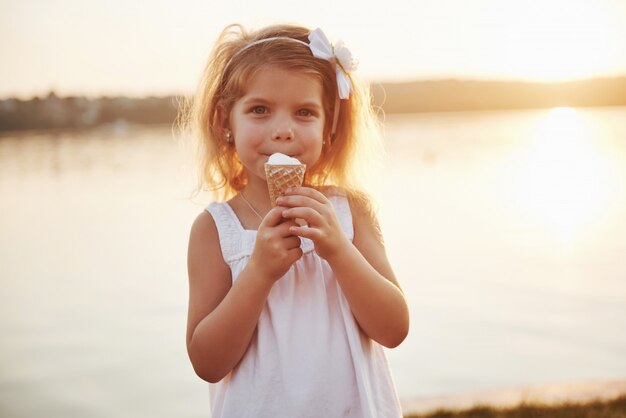 Una hermosa niña come un helado cerca del agua