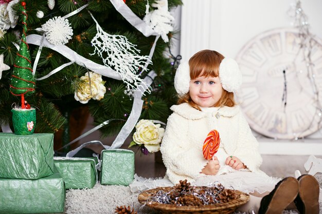 Hermosa niña comiendo una piruleta. Retrato de una niña graciosa en orejeras con un delicioso caramelo en las manos. Concepto de Navidad y año nuevo