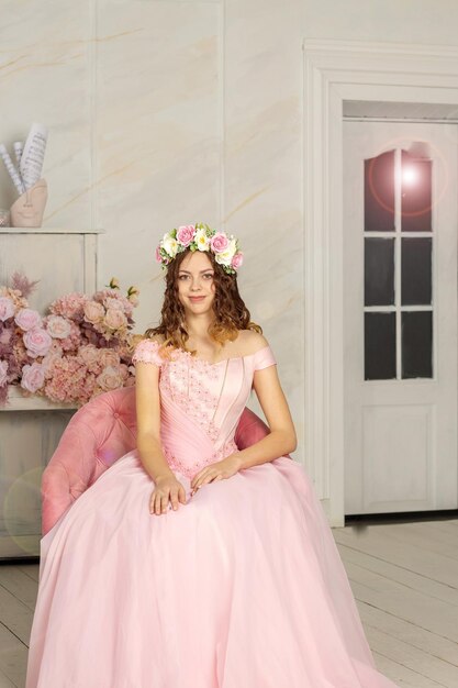 Una hermosa niña con una corona de flores en la cabeza y un vestido largo rosa es fotografiada en un estudio fotográfico Spring PHOTOSESSION