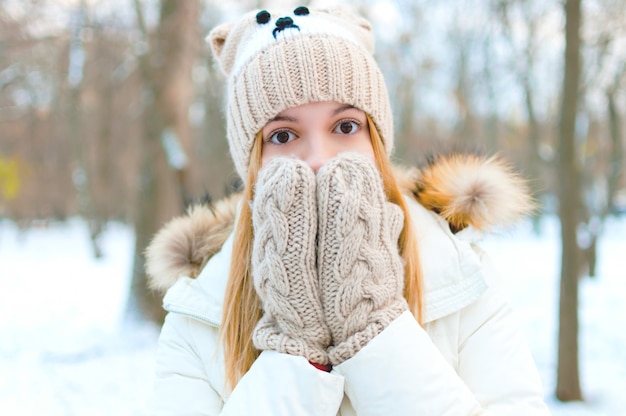 Foto una hermosa niña se cubre la boca con las manos en guantes. bosque de invierno, ambiente navideño.