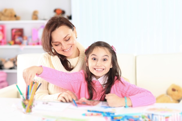 Hermosa niña dibuja con su mamá en casa sentada en el sofá