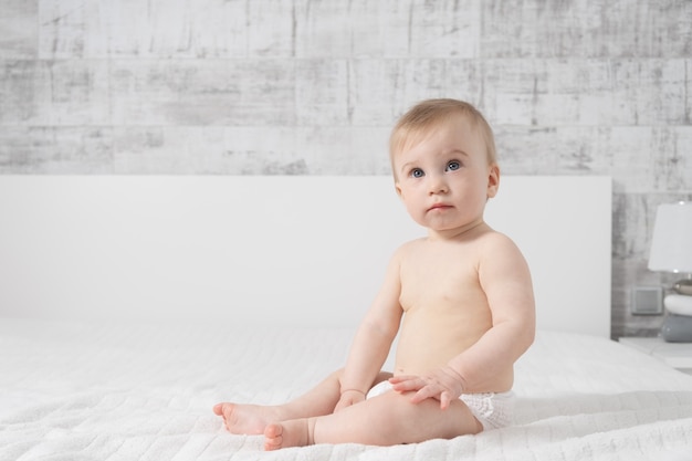 Hermosa niña de diez meses sentada en la cama en el interior en luz interior moderno. Concepto de infancia feliz.