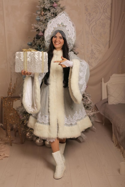 una hermosa niña con un disfraz de doncella de nieve sostiene una caja de regalo en el árbol de Navidad