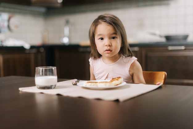 Foto hermosa niña de dos años está esperando que la comida comience a mirar a la cámara