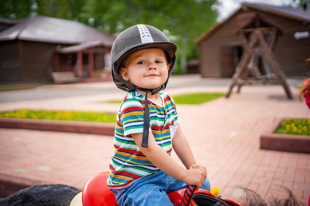 Hermosa niña de dos años montando caballo pony en un gran casco de jockey de seguridad posando al aire libre en