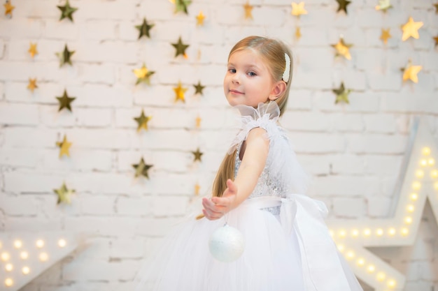 Hermosa niña elegante con un vestido blanco con una bola de Navidad
