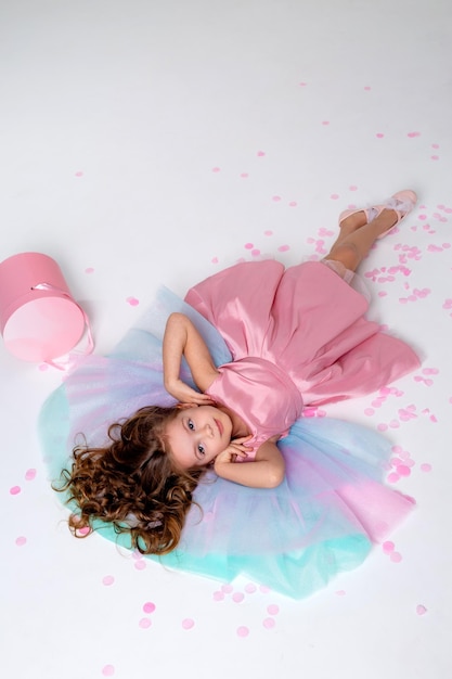 Hermosa niña con un elegante vestido rosa yace en el suelo cubierto de confeti vista superior moda