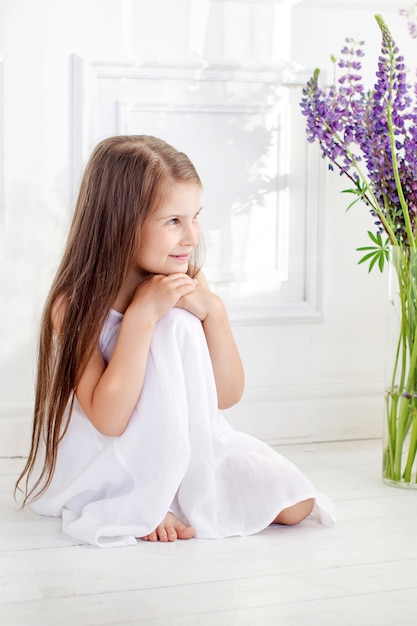 Hermosa niña emocional emplazamiento entre flores violetas. Una decoración de flores en un interior.