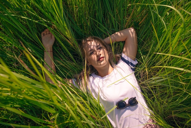 Foto hermosa niña se encuentra en la hierba en camiseta blanca en blanco en la hierba