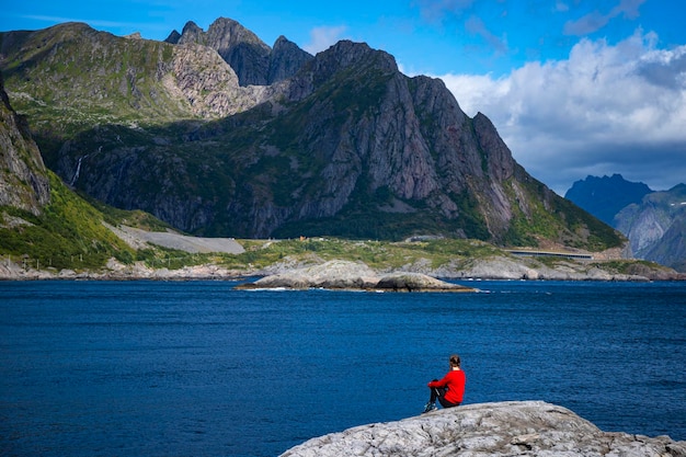 Una hermosa niña se encuentra en las rocas sobre el mar con vistas a las poderosas montañas de noruega