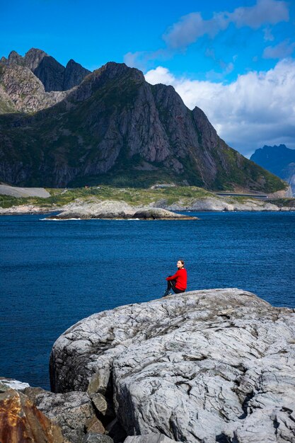 Una hermosa niña se encuentra en las rocas sobre el mar con vistas a las poderosas montañas de noruega
