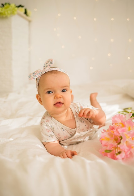 Hermosa niña se encuentra en traje junto a flores en la cama