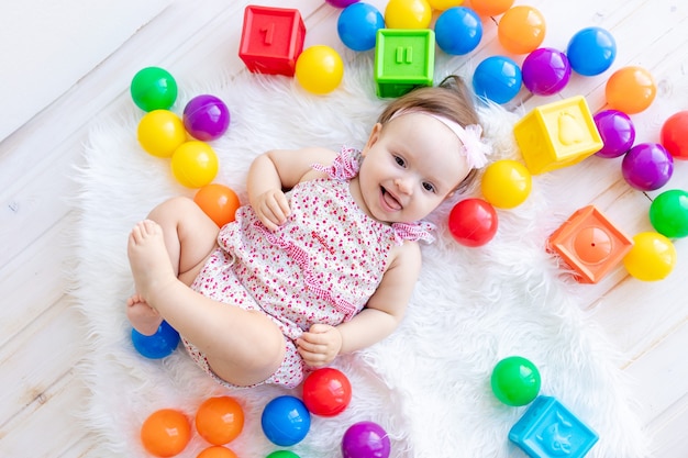 Una hermosa niña está mintiendo en ropa roja sobre una alfombra blanca entre cubos y bolas de juguetes