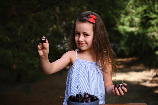 Hermosa niña europea con tazón de bayas de cereza en el jardín del campo