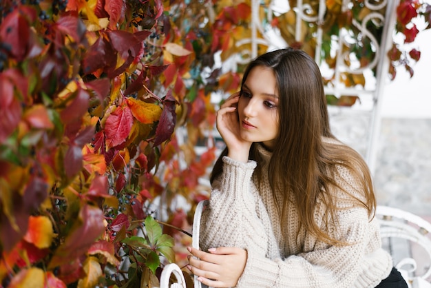 Una hermosa niña feliz con cabello castaño claro entre hojas amarillas y rojas en un parque de otoño.