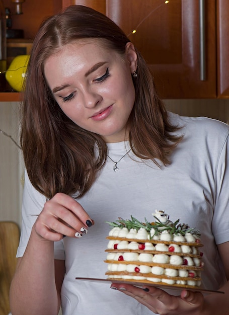Una hermosa niña feliz con una camiseta blanca se para en casa con un pastel festivo de Año Nuevo en un plato