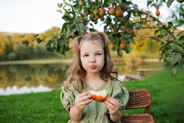 Foto una hermosa niña feliz con un vestido verde está comiendo una pera