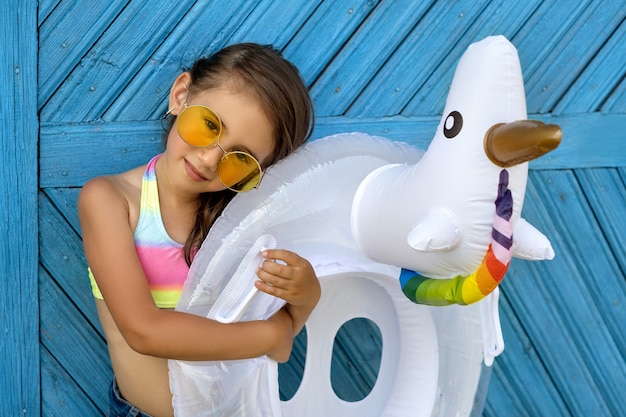 Una hermosa niña con gafas de sol está de pie junto a una pared azul con un círculo en forma de unicornio