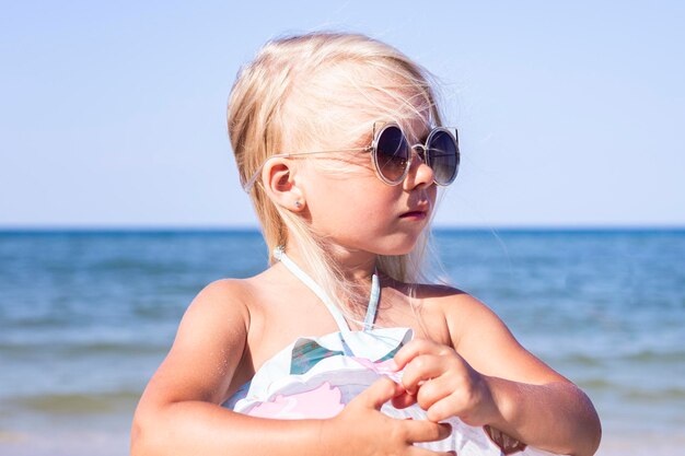 Hermosa niña con gafas de sol en la playa en un día soleado