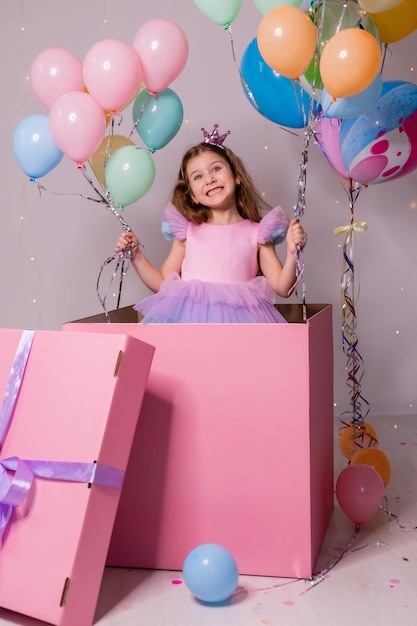 Hermosa niña con globos salta de una enorme caja rosa niño celebra su cumpleaños