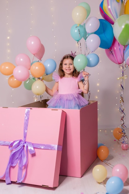 Hermosa niña con globos salta de una enorme caja rosa niño celebra su cumpleaños