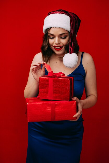 Una hermosa niña con un gorro de Papá Noel tiene un regalo de año nuevo en sus manos sobre un fondo rojo.