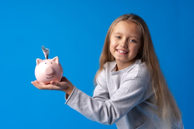 Hermosa niña con hucha sobre fondo azul.