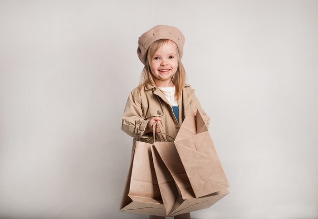 Una hermosa niña con un impermeable beige y una boina con bolsas de papel