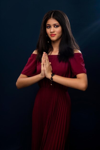 Hermosa niña india con expresión de bienvenida o invitando o saludando a Namaste en un fondo gris