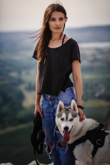 Foto hermosa niña juega con un perro, husky gris y blanco, en las montañas al atardecer. niña india y su lobo