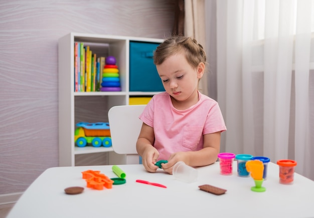 Hermosa niña jugando con arcilla en la mesa de la habitación