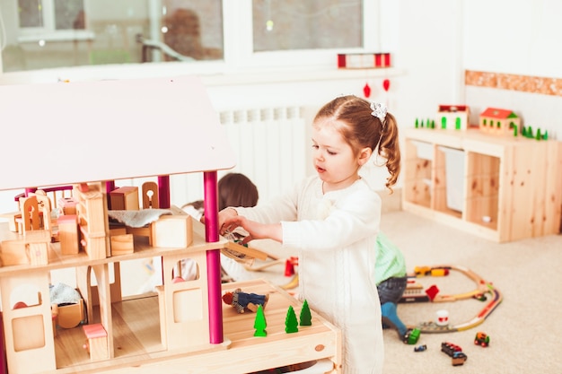 Hermosa niña jugando con una casa de muñecas de madera