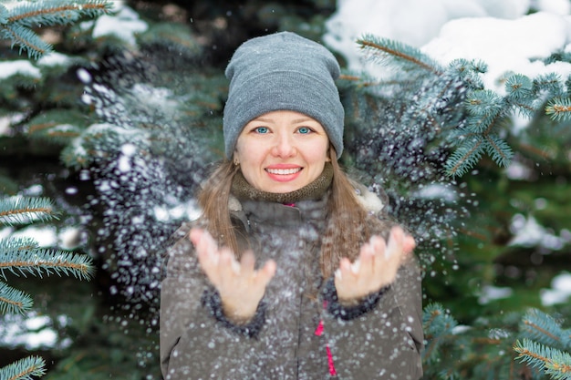 Hermosa niña jugando con nieve, divirtiéndose en el parque de invierno. mujer joven feliz disfrutando de la naturaleza al aire libre. Invierno